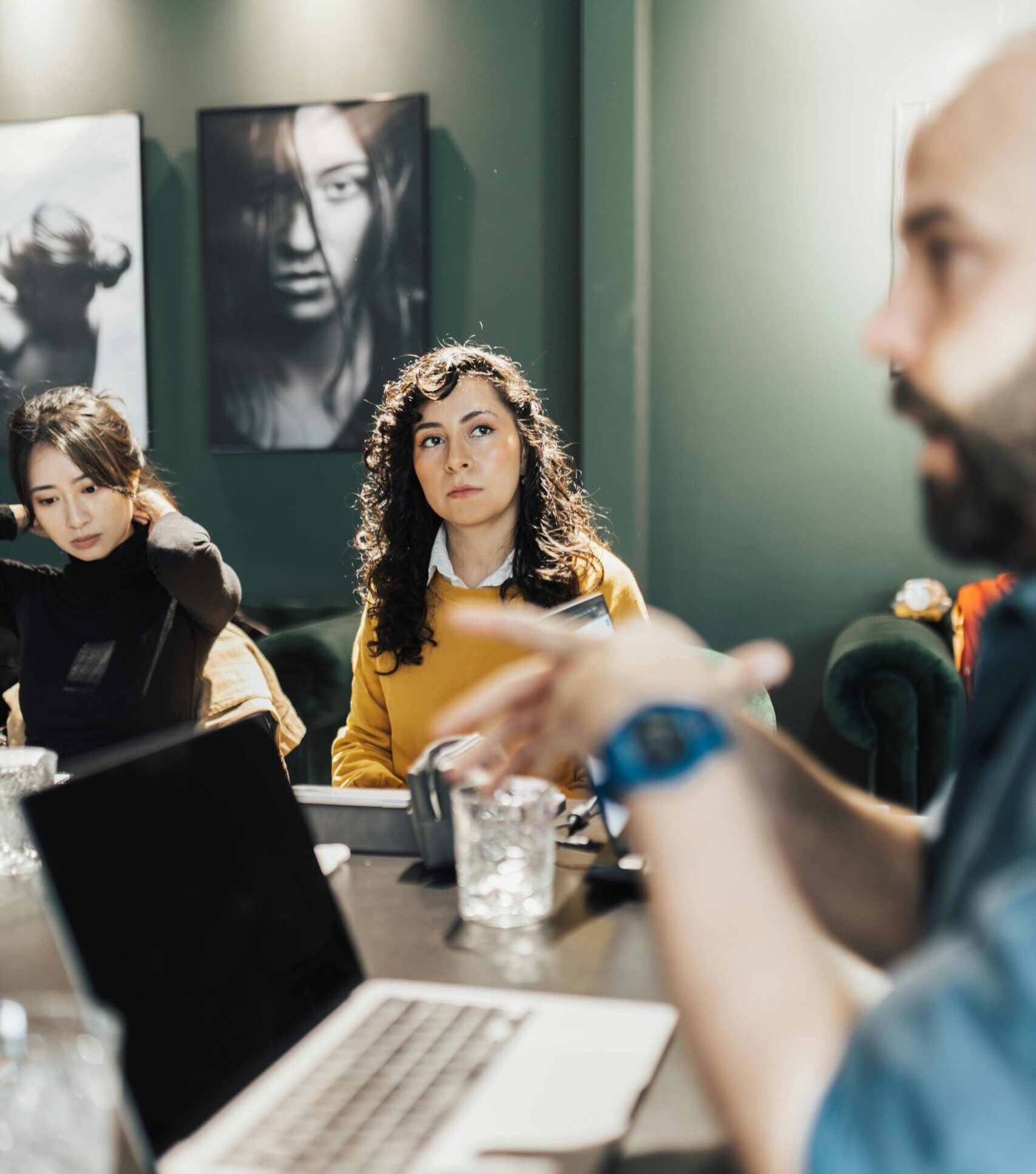Professionals discussing projects around a conference table with laptops and notepads in an office.